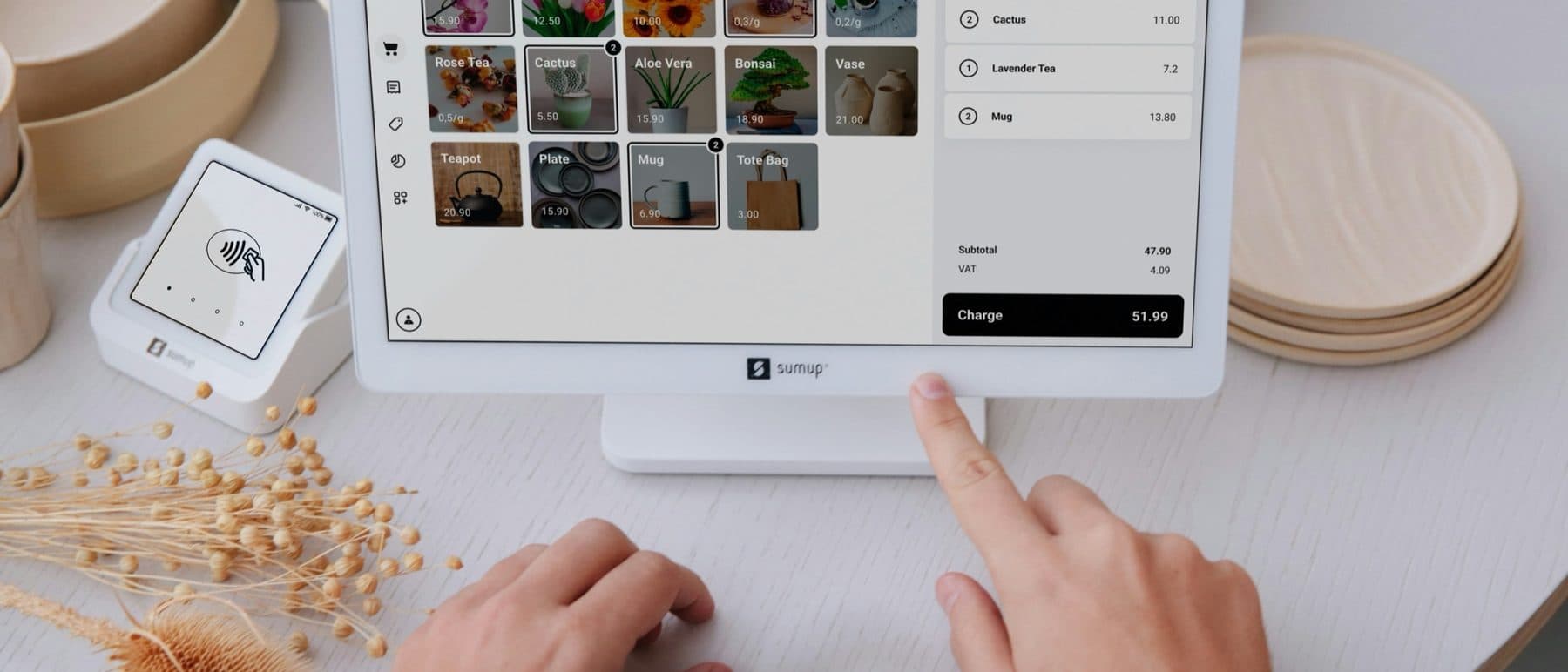An overhead view of hands ringing up a sale on a point-of-sale tablet in a small shop